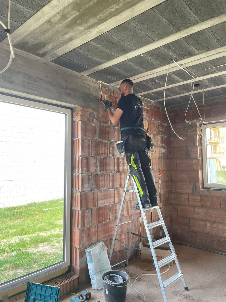 Instalator WOB Tech na drabinie podczas prac przy przewodach w domu w Zaklikowie