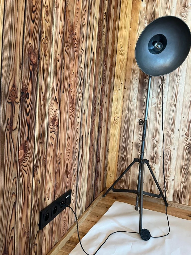 Czarna lampa stojąca i gniazda elektryczne na drewnianej ścianie domu z bali